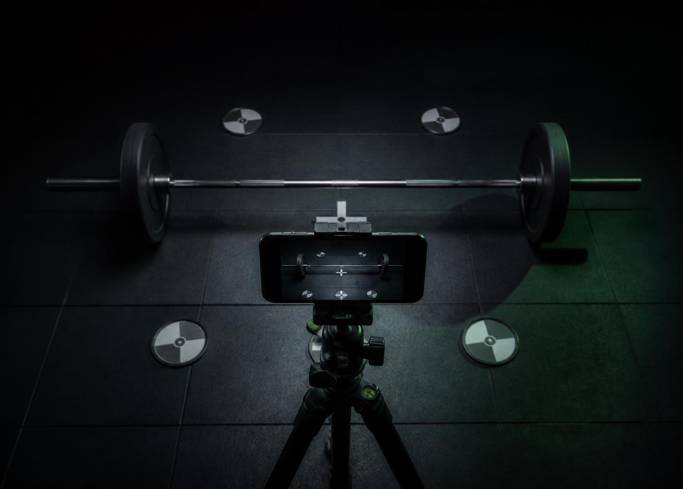 Phone on a tripod framing a barbell with floor calibration markers