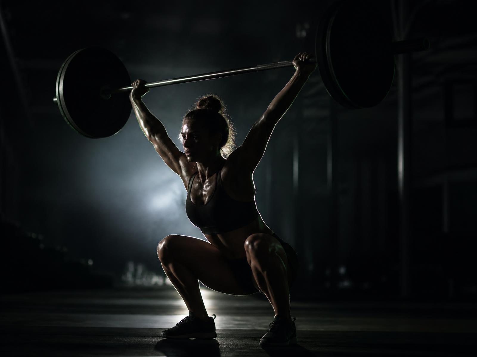 Athlete locking out a barbell overhead in a dark gym